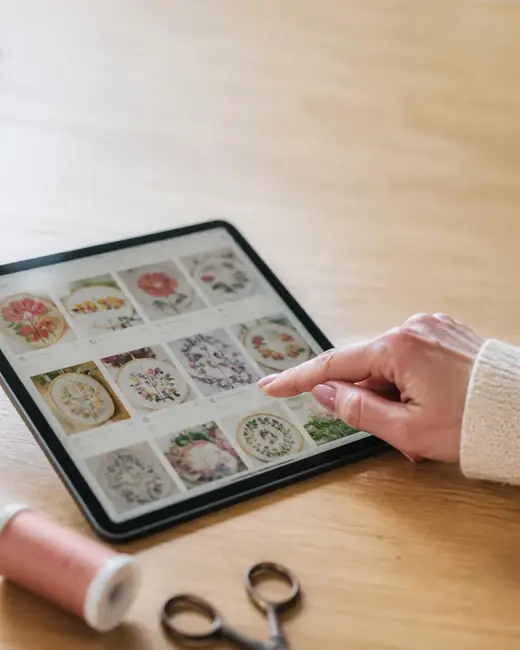 Mão a escolher um risco de bordado numa biblioteca digital num tablet